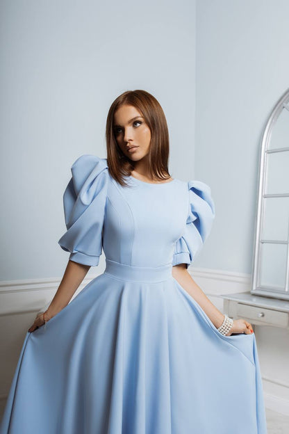 Woman wearing a light blue dress with puffed sleeves in an elegant room.