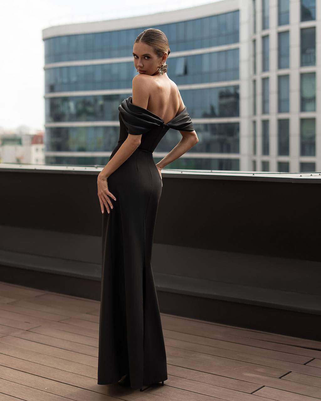 Woman in a black evening gown on a rooftop with modern building in the background