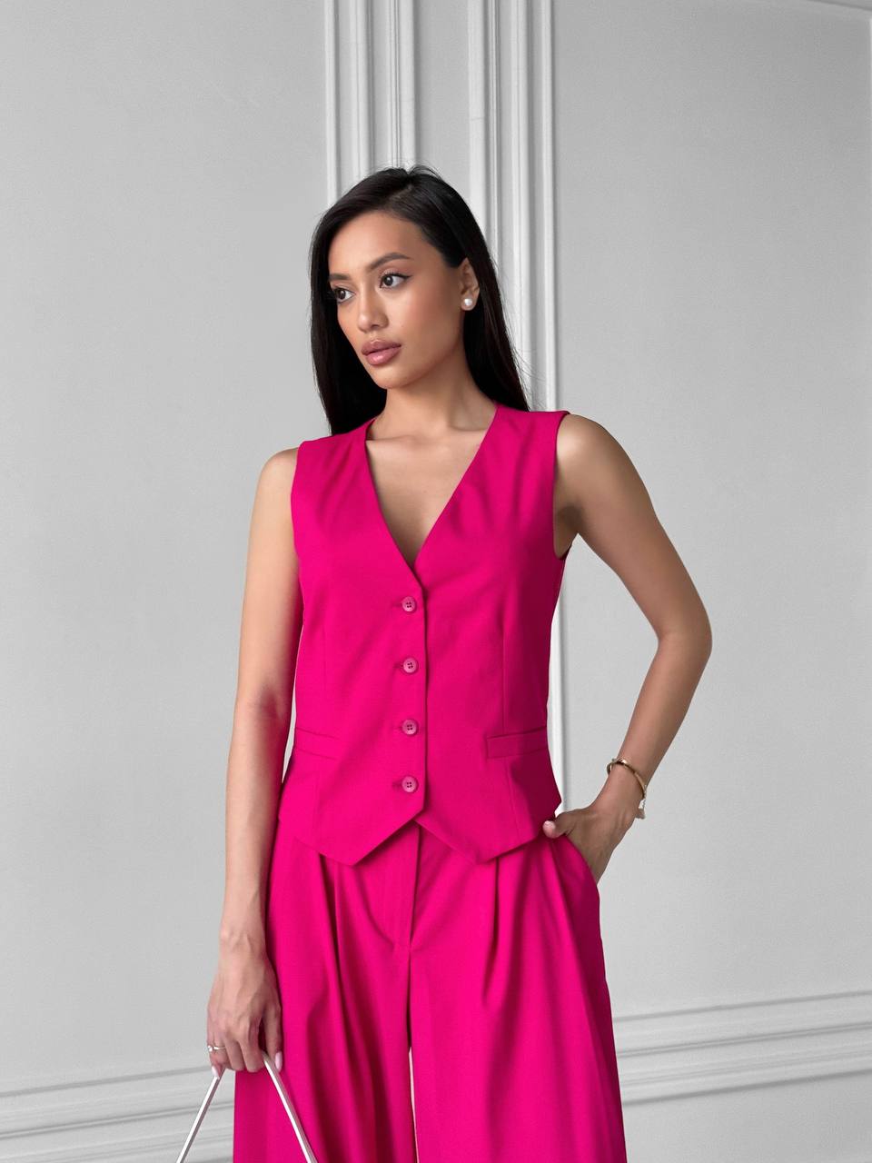 Woman wearing a bright pink sleeveless top and pants against a light gray background