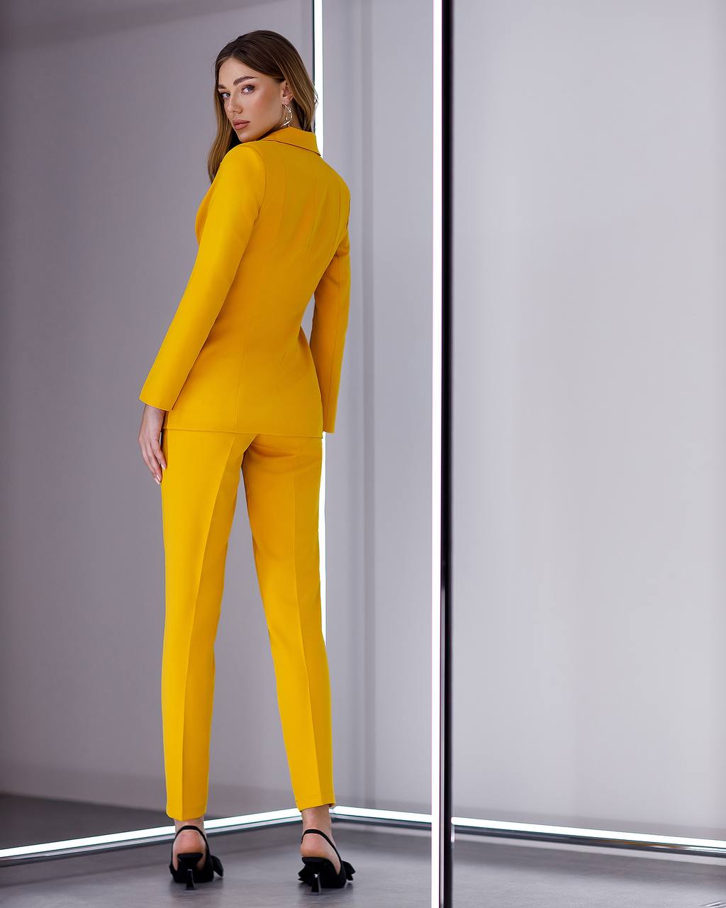 Woman wearing a yellow suit standing in front of a mirror.