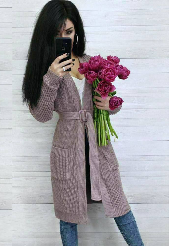 Woman in a long pink coat holding a bouquet of pink roses against a white wooden panel background