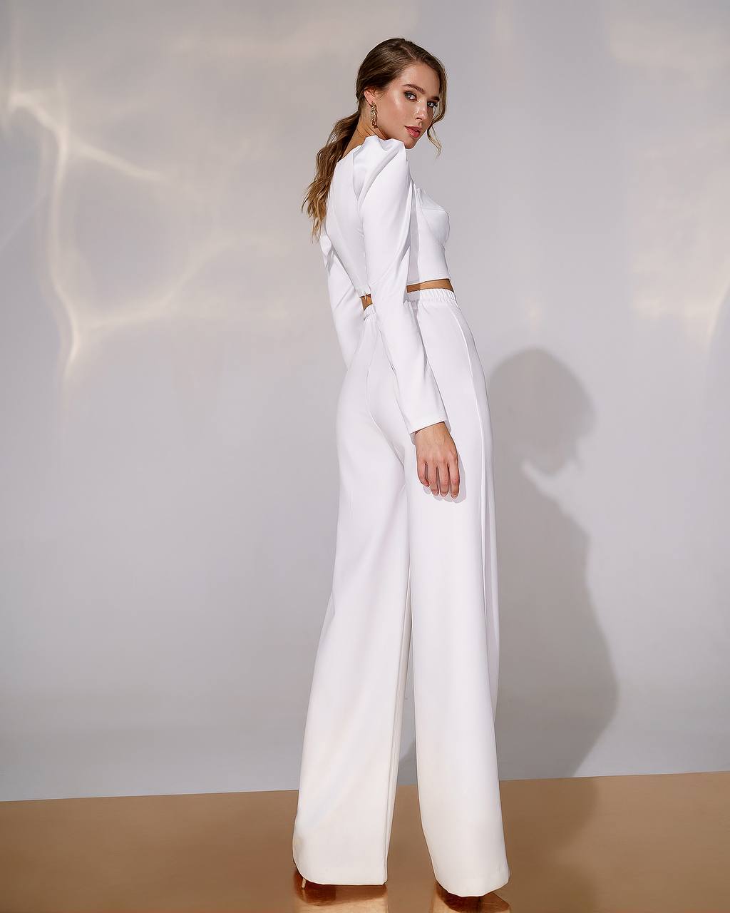 Woman wearing a white outfit with a high collar against a neutral background