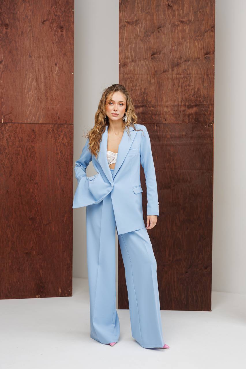Woman wearing a light blue suit standing against a wooden panel background