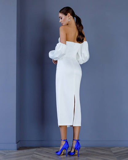 Woman in a white off-shoulder dress with puffed sleeves against a blue wall.