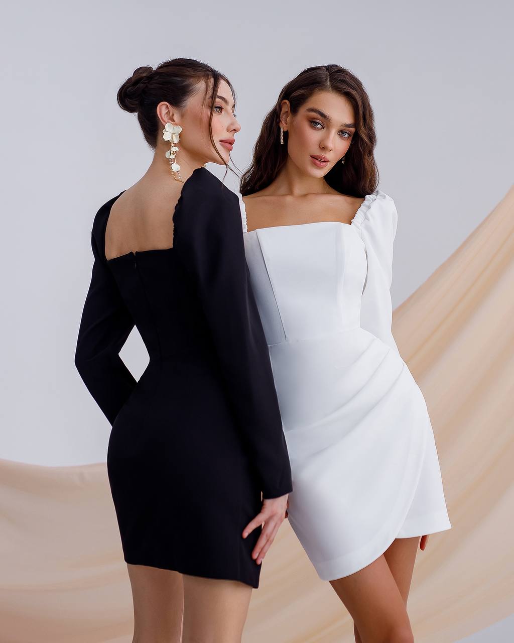 Two women wearing black and white dresses against a neutral background