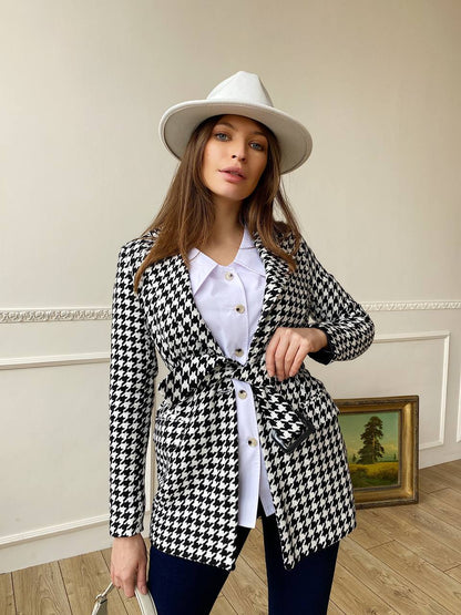 Woman wearing a black and white checkered jacket with a white hat indoors.