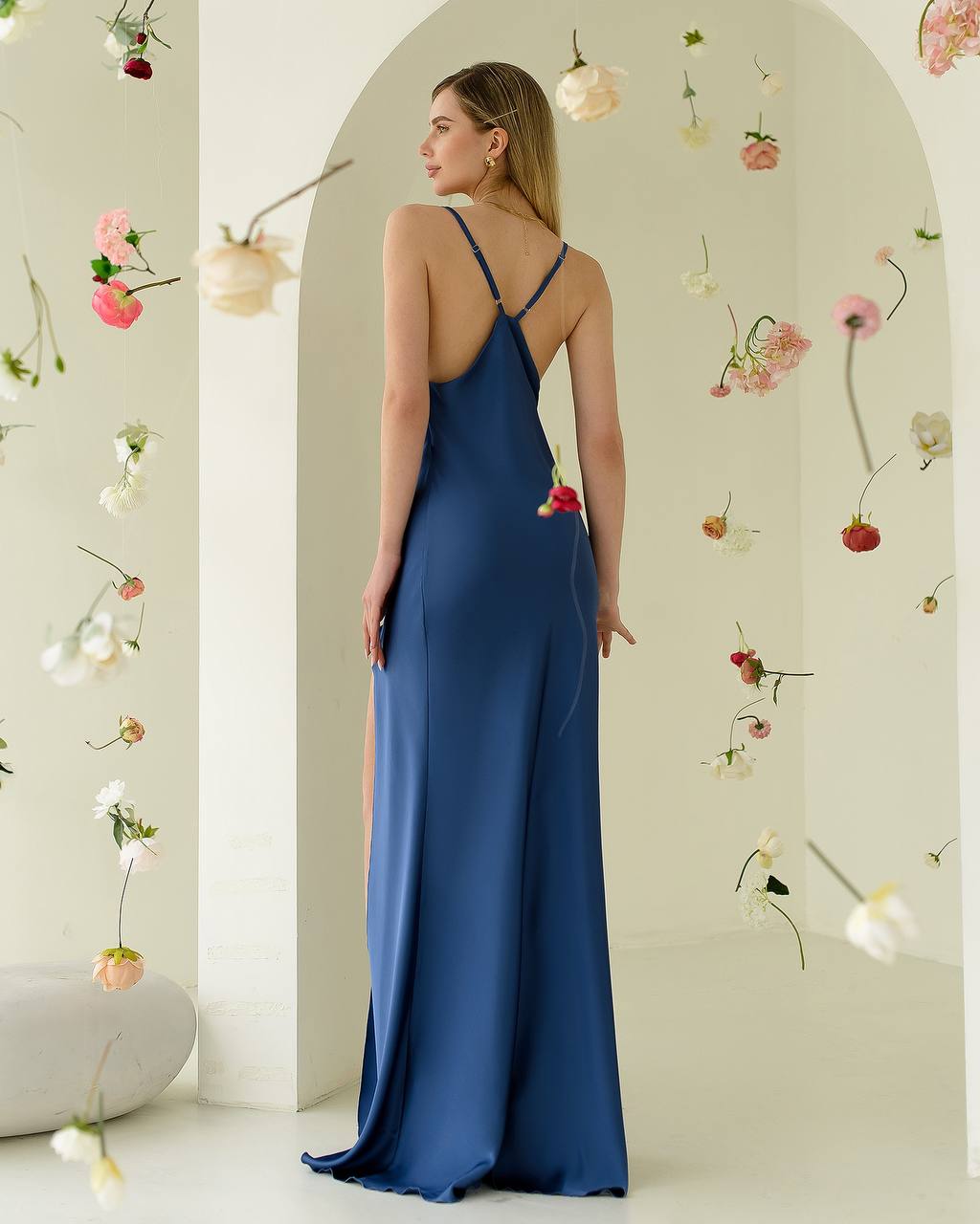 Woman in a blue evening gown standing in front of a floral decorated archway.