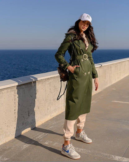 Woman in a green trench coat standing by the ocean