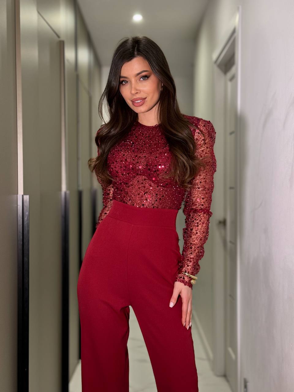 Woman in a red sequin top and high-waisted pants standing in a hallway.