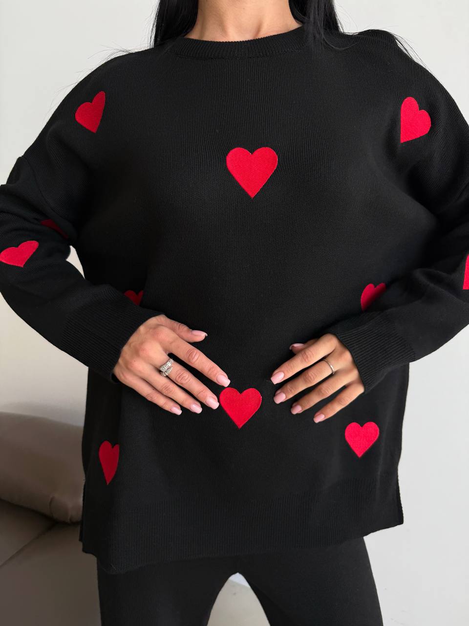Black sweater with red heart patterns worn by a person.