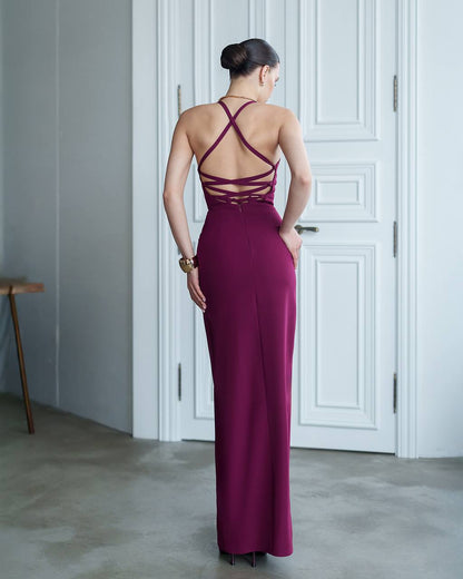 Woman wearing a burgundy evening gown with a backless design in a room with white walls and a door.