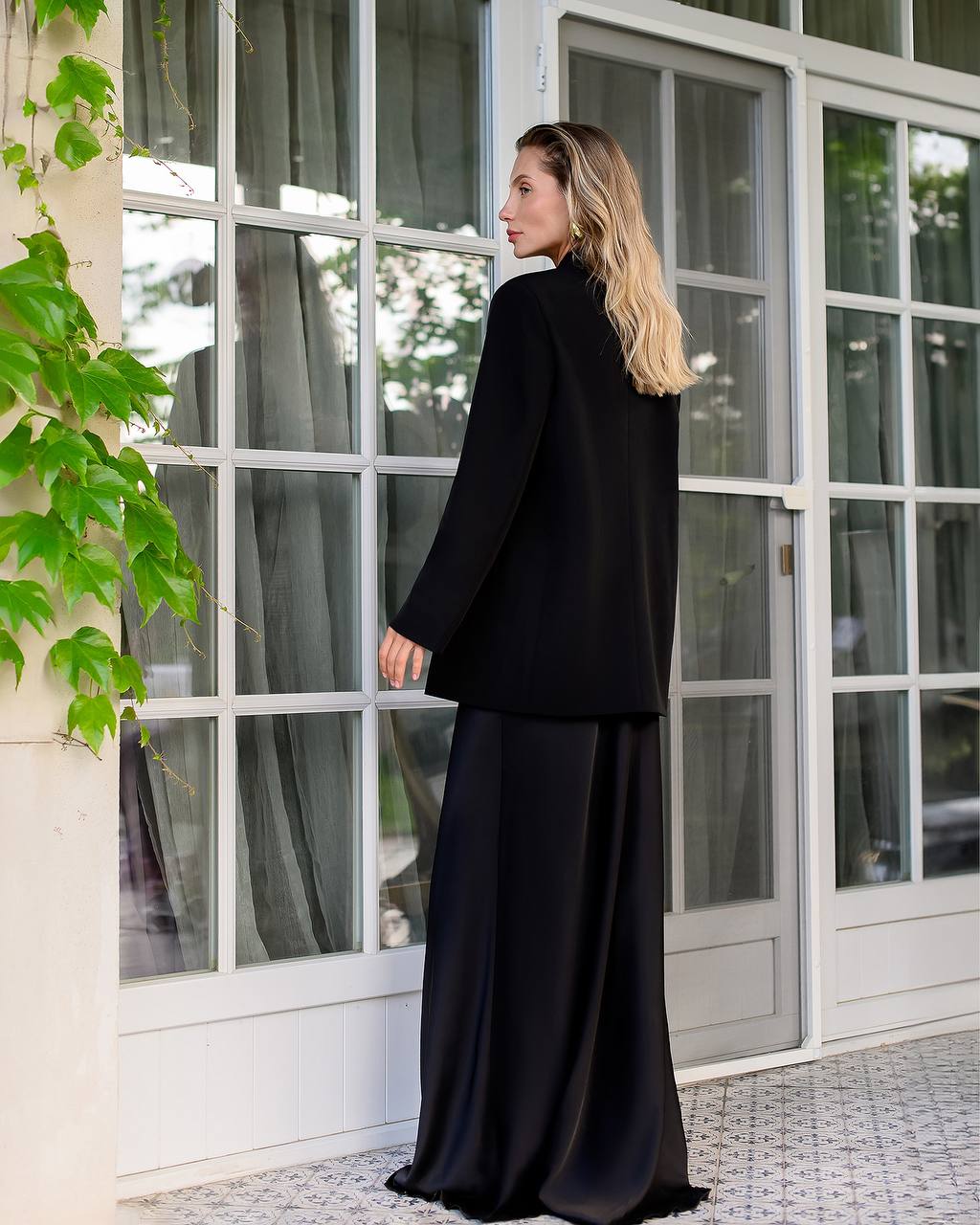 Woman in a black outfit standing in front of a large window with greenery.