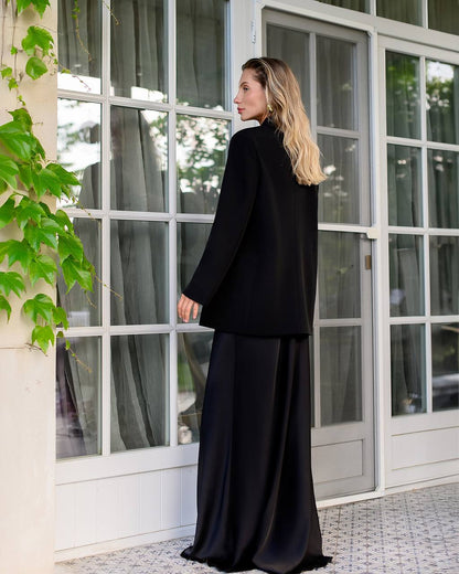 Woman in a black outfit standing in front of a large window with greenery.