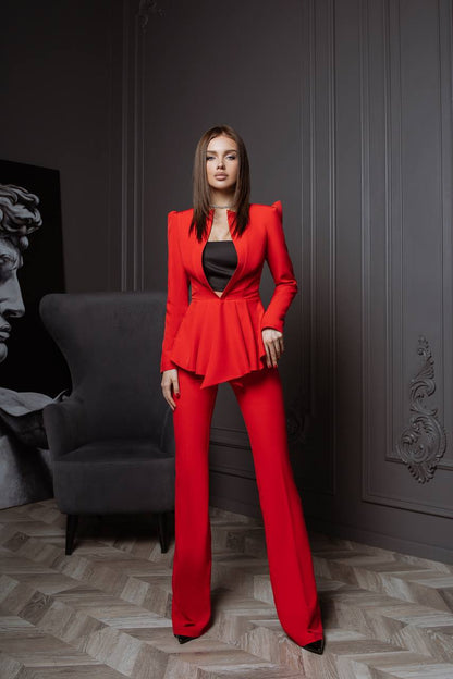 Woman in a red suit standing in a room with gray walls and a gray chair.