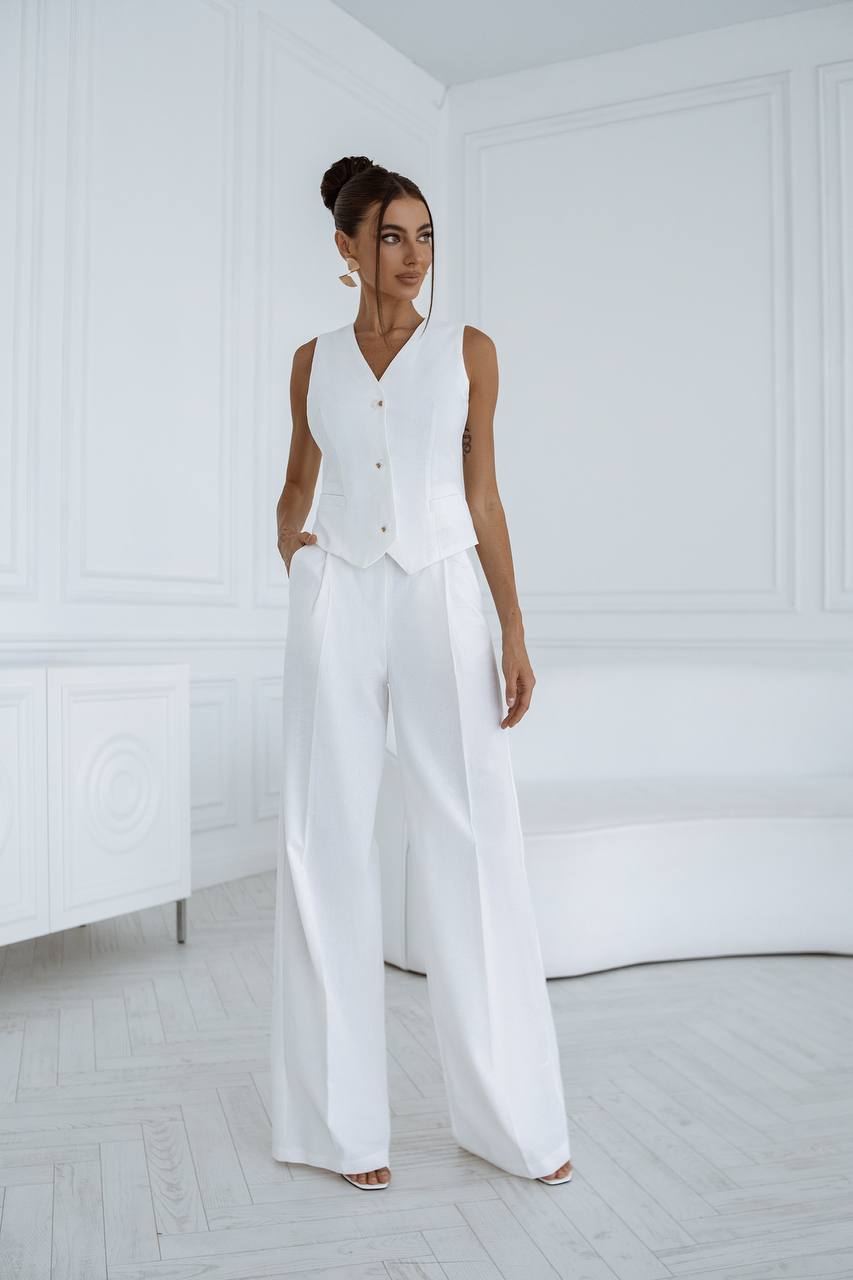 Woman wearing a white sleeveless top and wide-leg pants in a minimalistic room.