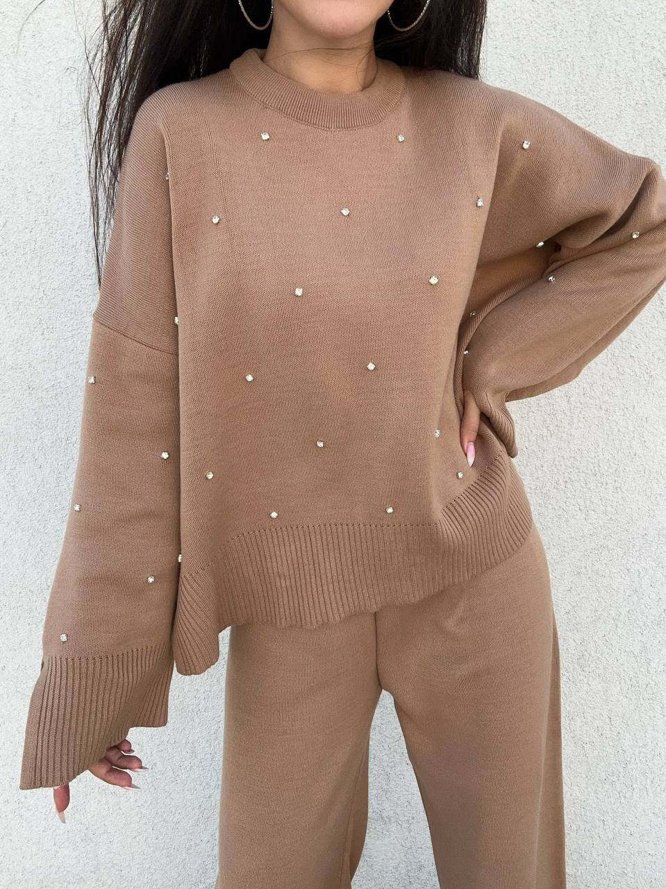Brown sweater with pearl embellishments worn by a person against a light gray background