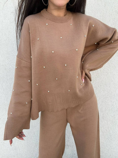 Brown sweater with pearl embellishments worn by a person against a light gray background