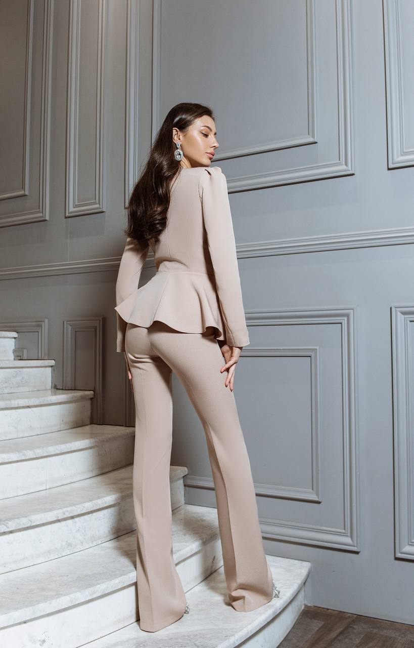Woman in a beige suit standing on a staircase with gray paneled walls.