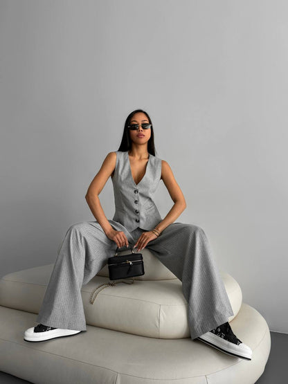 Woman in a gray outfit sitting on a white chair against a gray background