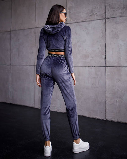 Woman wearing a gray tracksuit with a hood against a concrete wall.