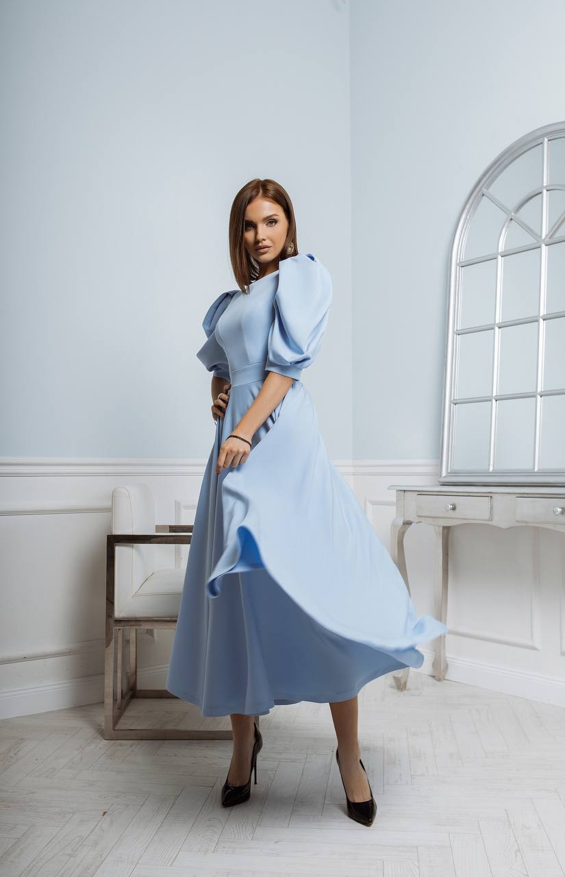Woman wearing a light blue dress in a room with white walls and a mirror.
