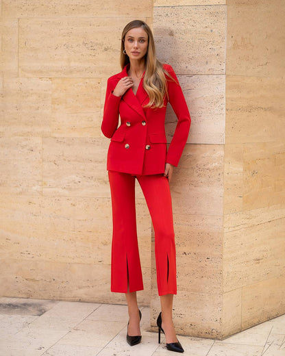 Woman in a red suit standing against a beige stone wall.