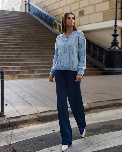 Woman wearing a blue cable knit sweater and dark blue pants walking on a city street.