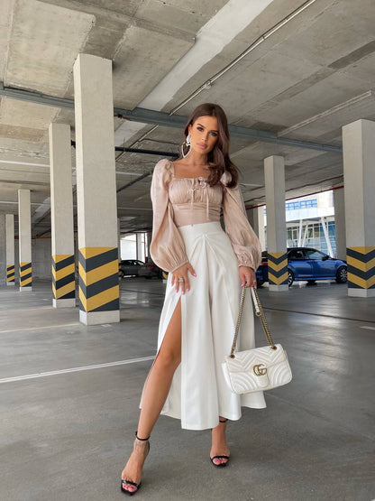 Woman in a stylish outfit with a white skirt and beige top in an indoor parking garage.