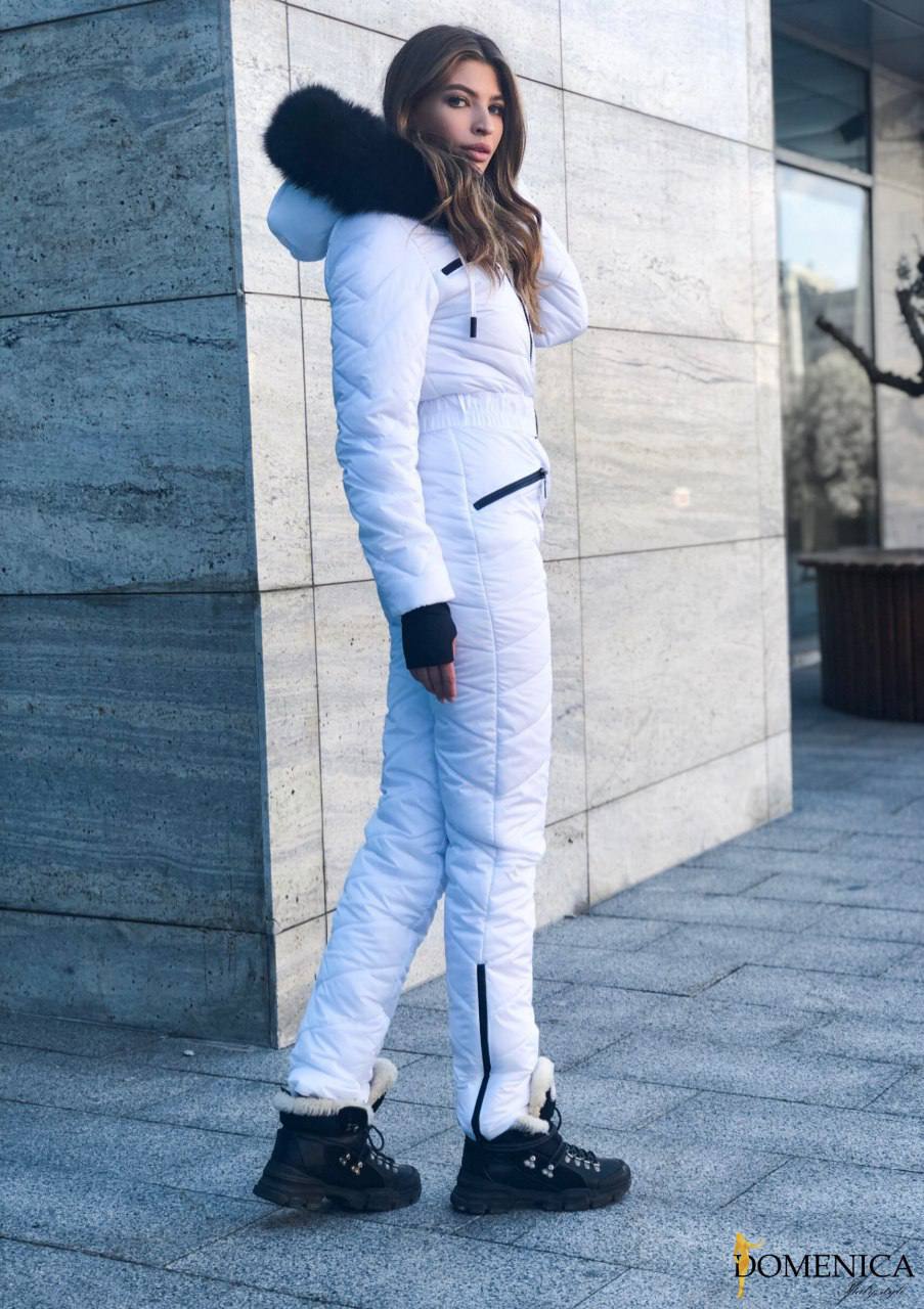 Person wearing a white snowsuit with black accents in front of a stone wall.