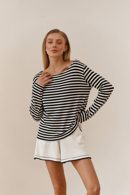 Woman wearing a black and white striped long-sleeve top and white shorts on a beige background