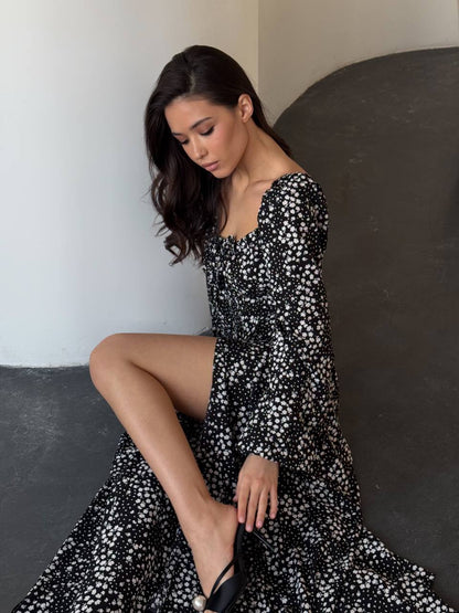 Woman in a black and white floral dress sitting on a dark surface.