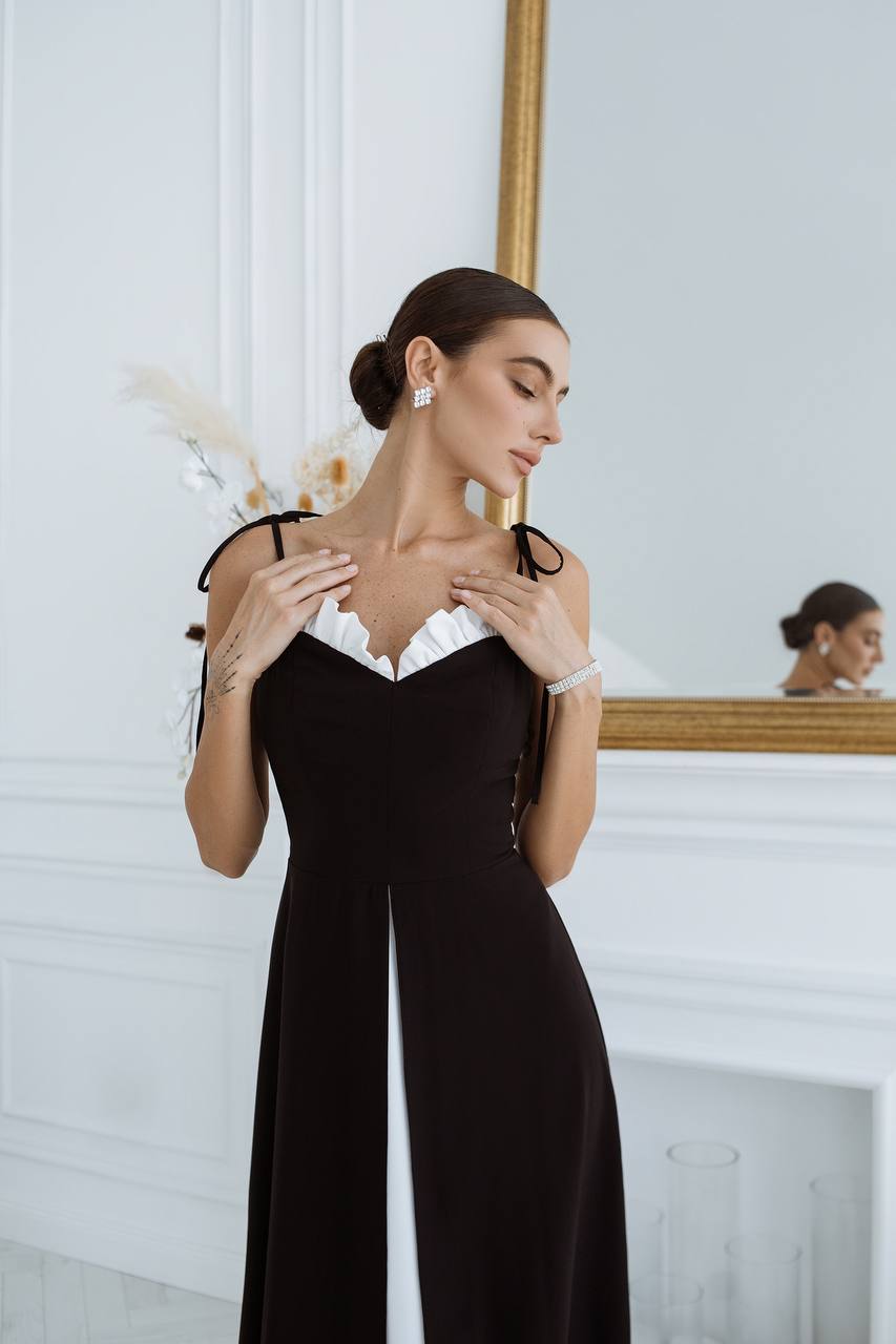 Woman in a black dress with white lace details standing in a room with a mirror.