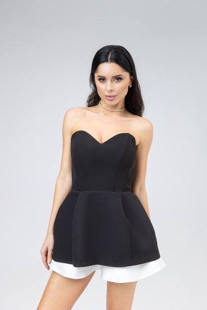 Woman wearing a black strapless dress with a white hem on a gray background