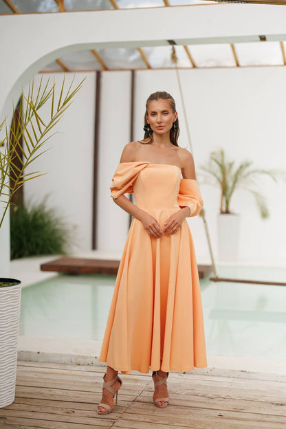 Woman in a peach off-shoulder dress standing in a modern indoor setting with plants.