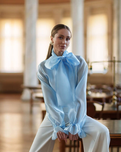 Woman wearing a light blue blouse with a large bow in an elegant indoor setting