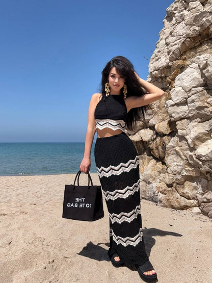 Woman in black and white striped outfit standing on a beach with ocean and rock wall in background