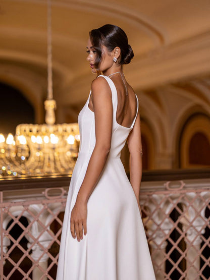 Woman in a white dress standing in an elegant indoor setting with chandeliers.