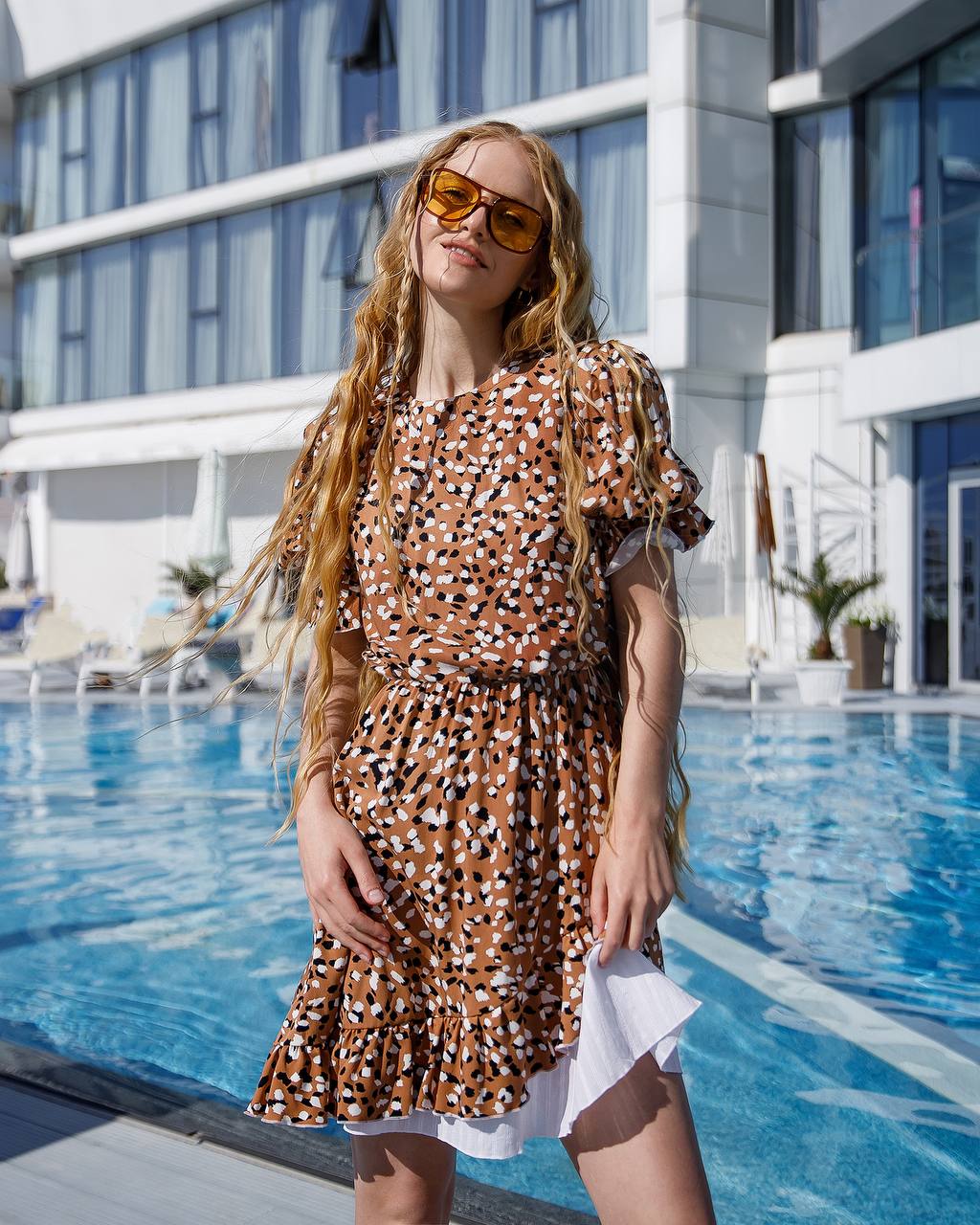 Woman in a patterned dress standing by a pool with a building in the background
