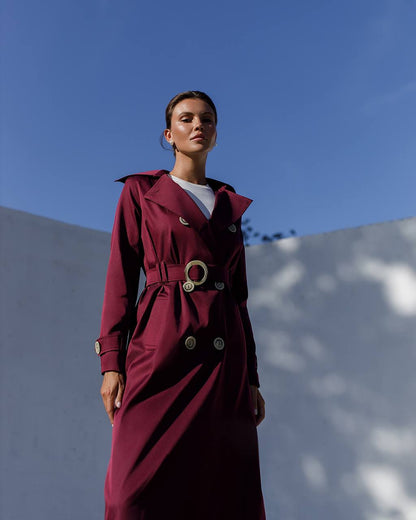 Woman wearing a burgundy trench coat against a blue sky