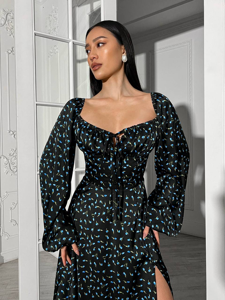 Woman wearing a black floral dress standing in a room with white walls.