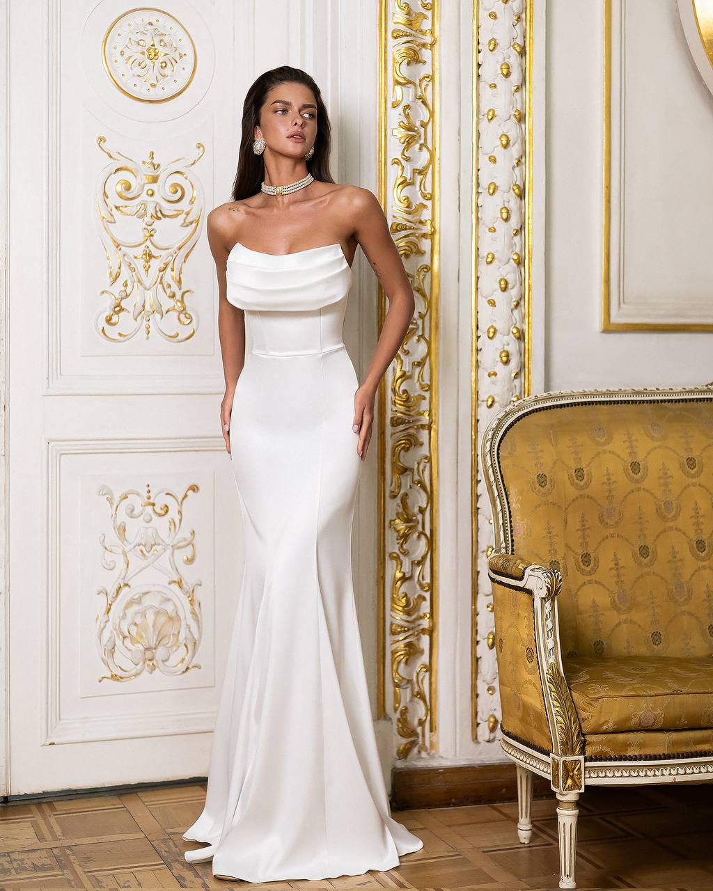 Woman in a white strapless gown standing in an ornate room with gold accents.