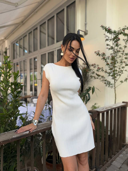 Woman in a white dress standing outdoors with plants and a building in the background