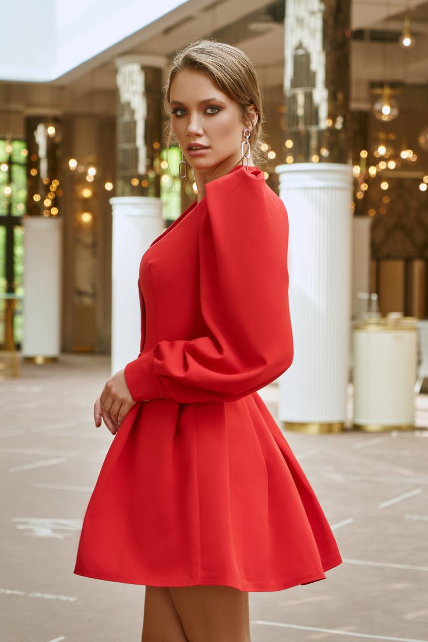 Woman wearing a red dress standing in an outdoor setting with columns and lights.