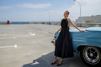 Woman in a black dress standing next to a blue vintage car on a parking lot.