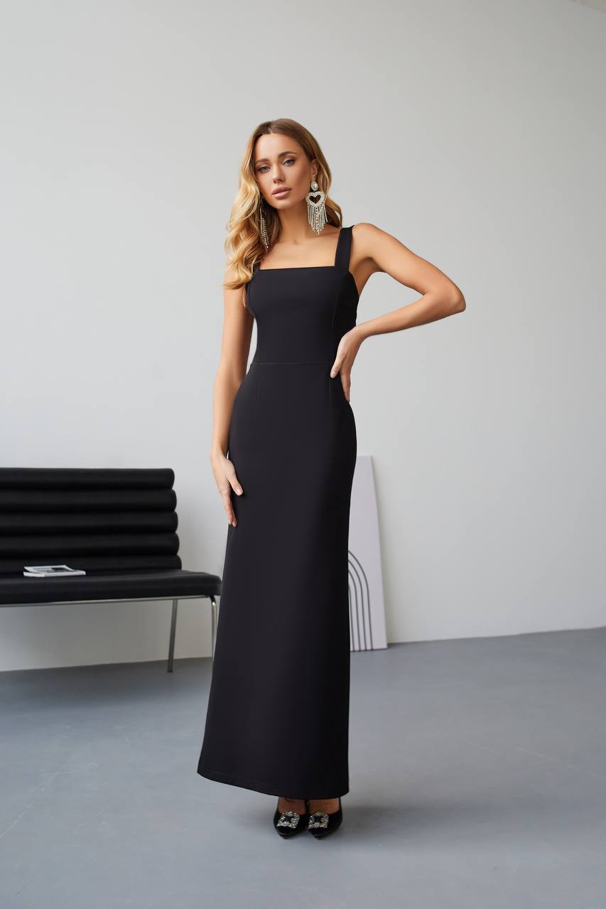 Woman wearing a black dress standing in a minimalistic room with a gray floor and white walls.