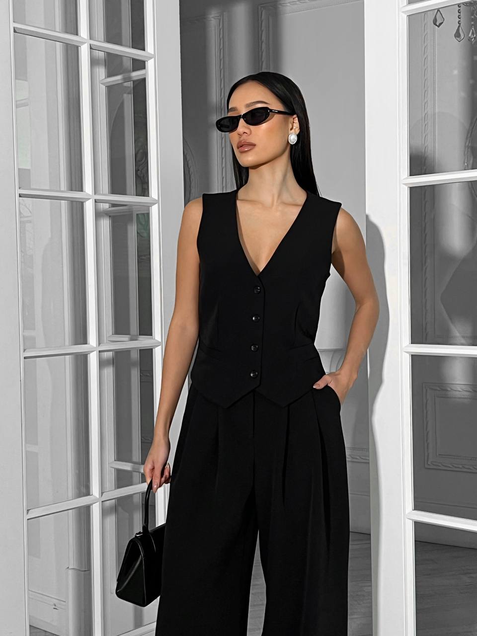 Woman wearing a black sleeveless top and pants in a room with white walls.