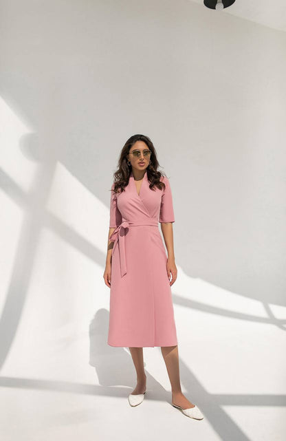 Woman wearing a pink dress standing in a well-lit room with white walls.