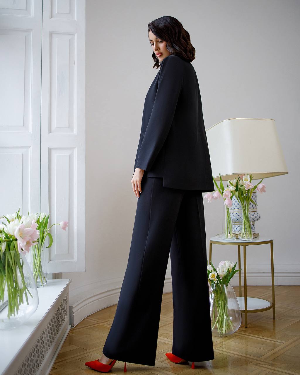Woman in a black outfit standing in a room with white walls and decorative elements.