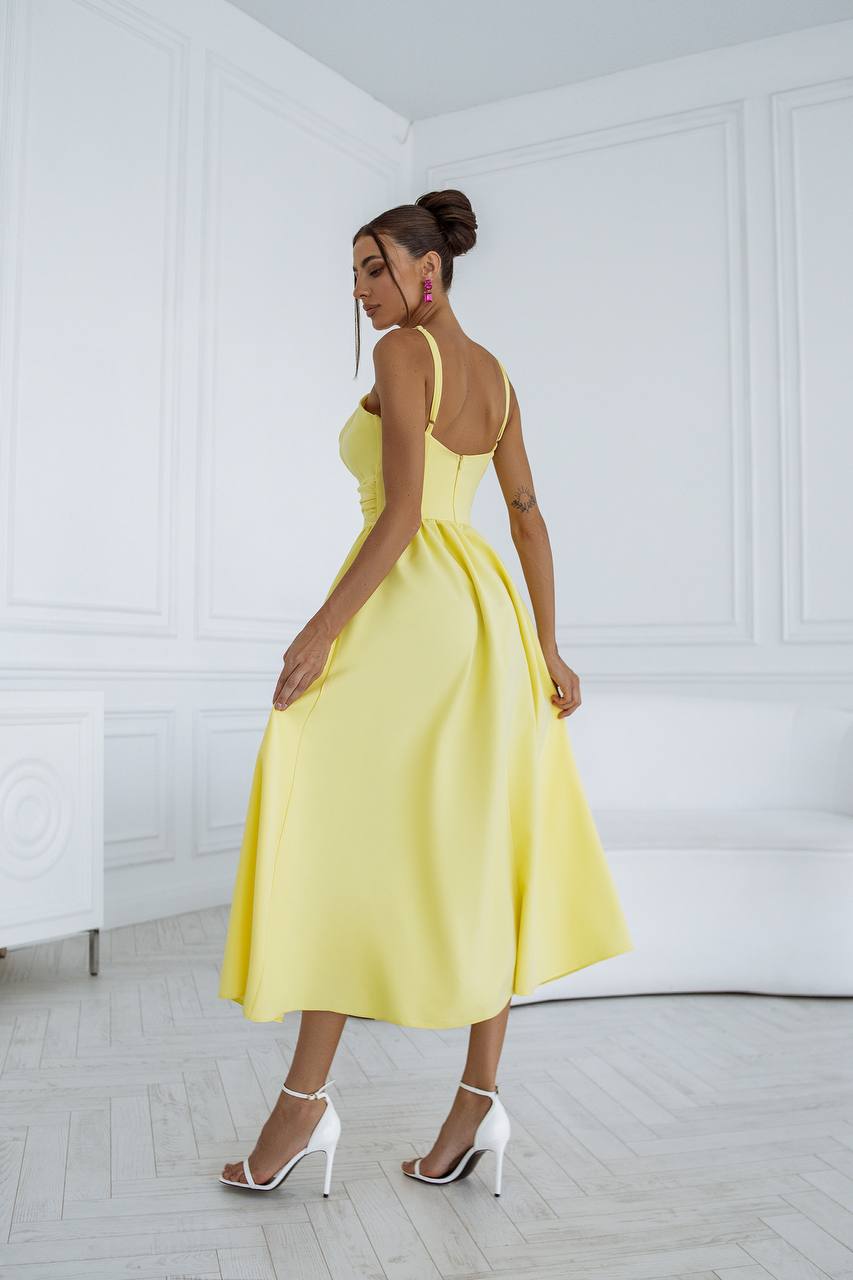 Woman in a yellow dress standing in a minimalistic room with white walls and floor.