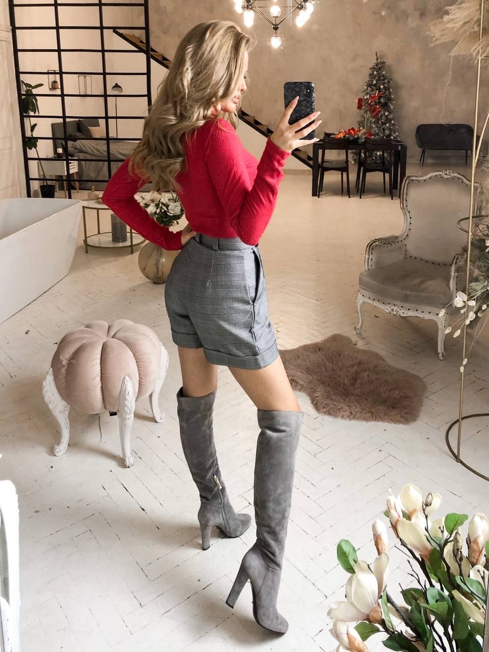 Woman taking a mirror selfie in a stylish room with decor elements.